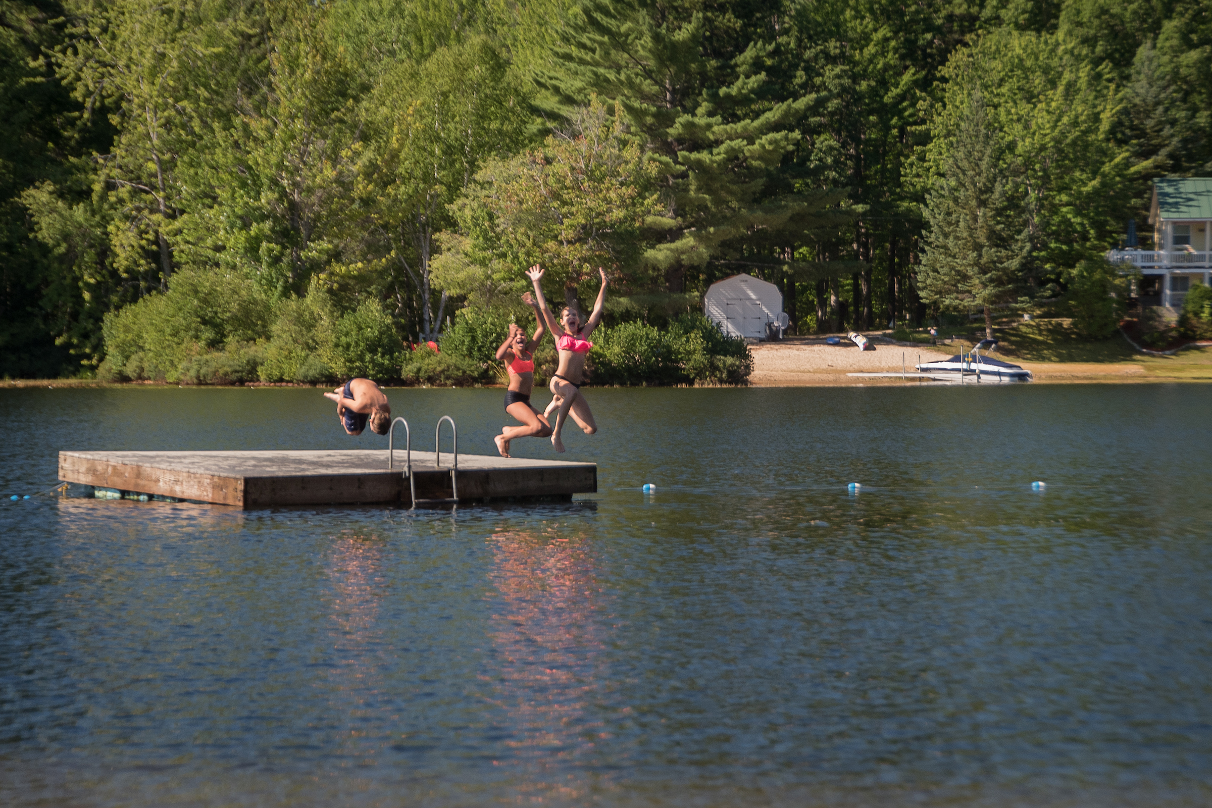 Three children jumping off a floating raft at Danforth Bay.